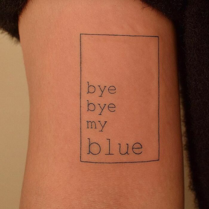 Minimalist word tattoo saying "bye bye my blue" in a simple rectangular outline on skin.