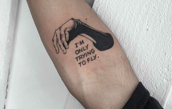 Arm with a unique word tattoo featuring a shaded hand and the phrase "I'm only trying to fly."