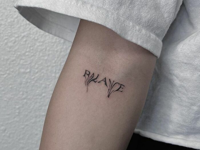 Word tattoo reading "Balance" on an arm, designed with leaf-like accents.