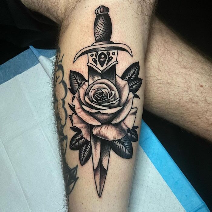 Calf tattoo featuring a detailed rose intertwined with a dagger, showcasing unique body art design.