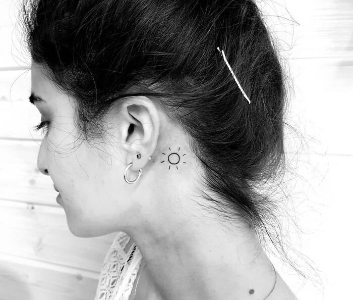 Female with a sun ear tattoo, hair pinned up, wearing earrings, showcasing minimalist ear tattoo design.