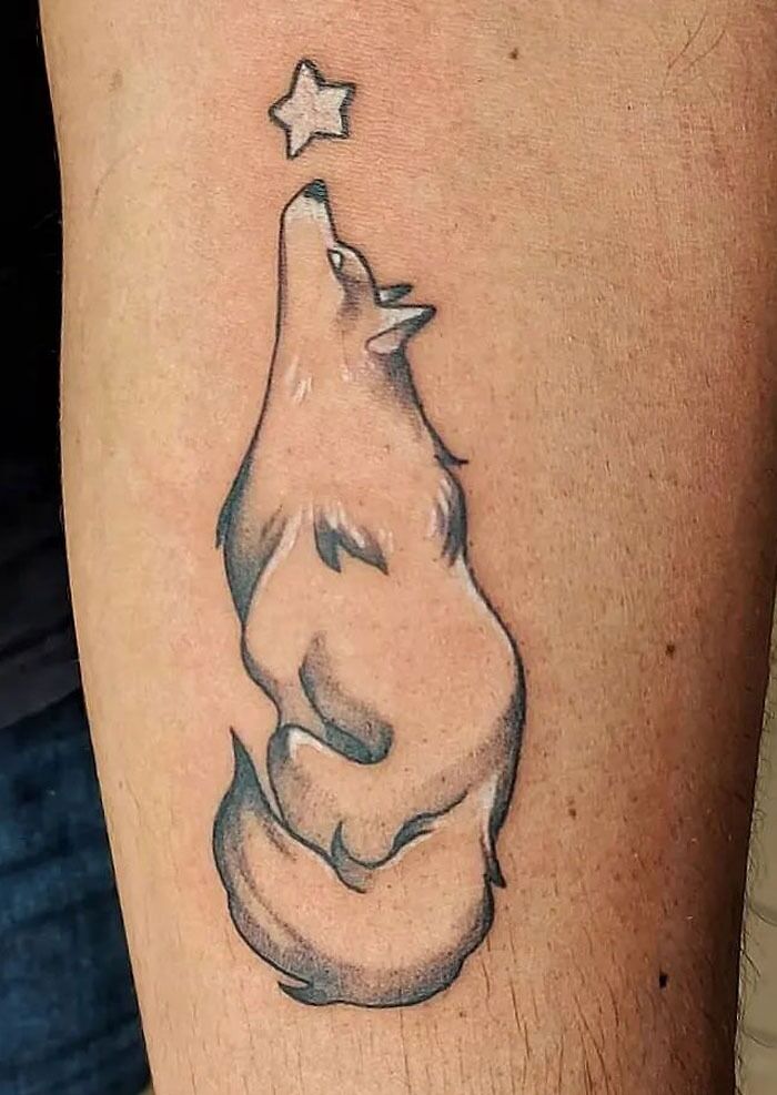 Wolf tattoo looking at a star, highlighting animal kingdom artistry on skin.
