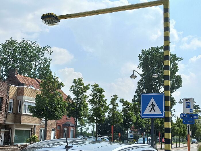 Innovative zebra crossing light in urban area with signs and parked cars nearby.