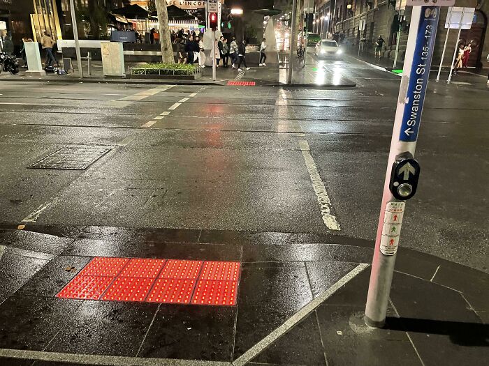 Crosswalk with tactile paving and pedestrian button, showcasing interesting city gadgets for accessibility at night.