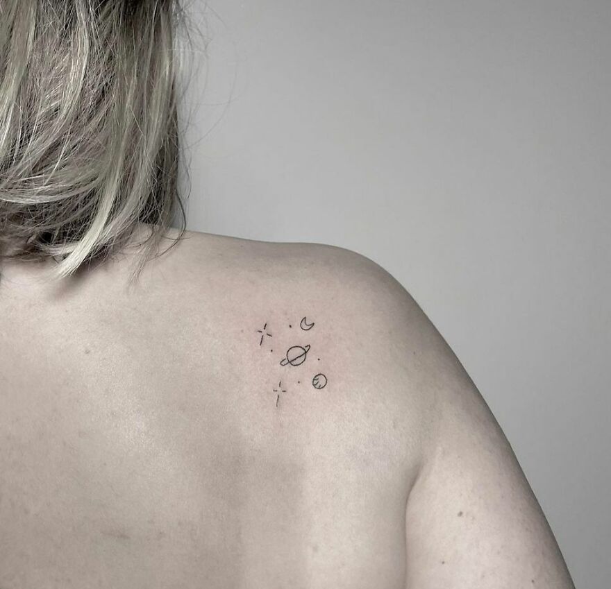 Minimalist space tattoos featuring planets and stars on shoulder skin.