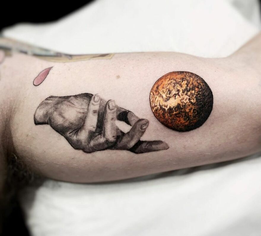 Tattoo of a realistic hand reaching for a planet, capturing the essence of outer space cool.