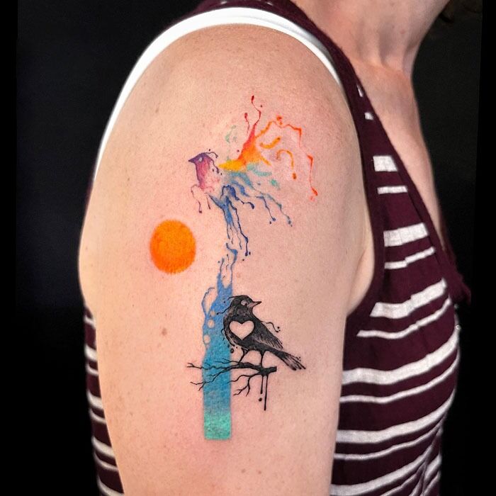 Colorful bird tattoo with a heart-shaped cutout celebrates the animal kingdom on an upper arm.