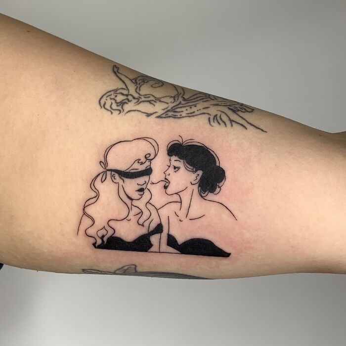 Illustrative tattoo of two women, one blindfolded, on an arm.