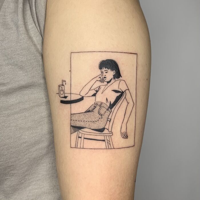 Illustration-like tattoo of a person sitting at a table, on an arm.