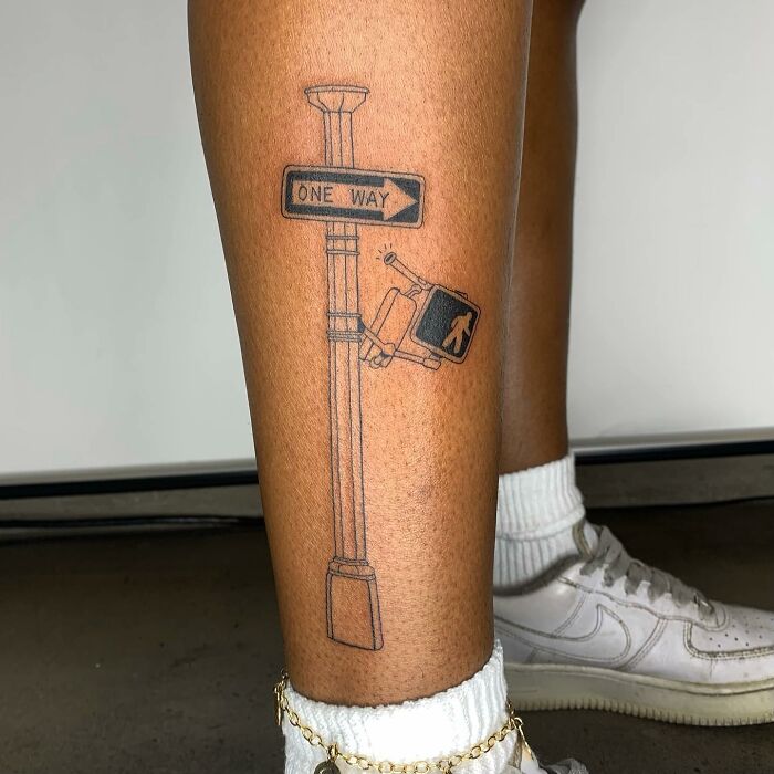 Stick figure tattoo on leg, resembling an illustration of a one-way signpost with a crosswalk signal.