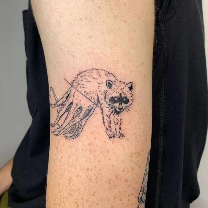 Illustrated-style tattoo of a raccoon with octopus legs on an arm.