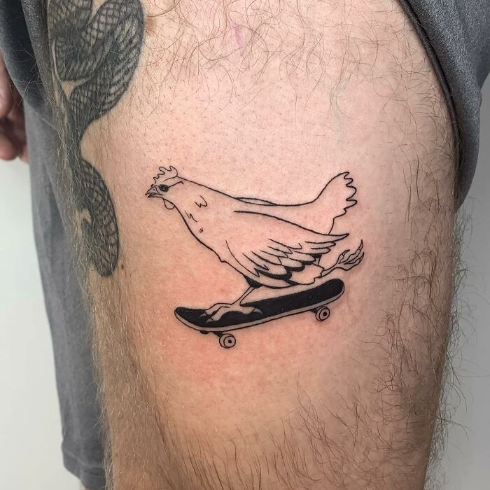 Illustration-style tattoo of a chicken on a skateboard on a person's thigh.