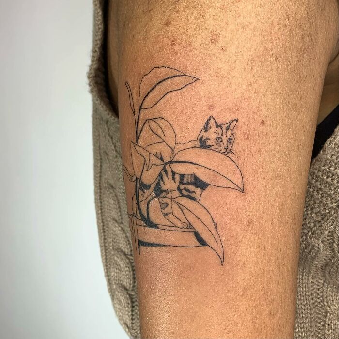 Illustrative tattoo of a cat hidden among leaves on a person's arm, showcasing intricate line work.