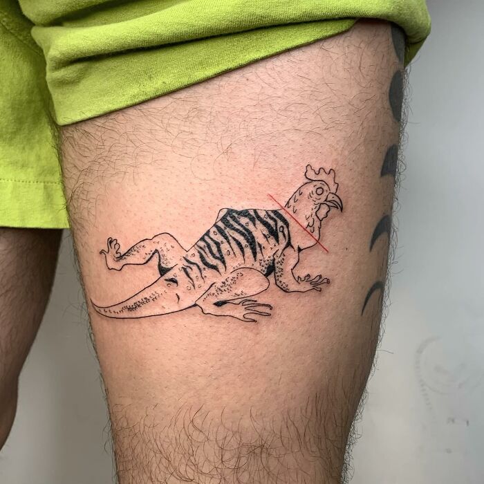 Illustration-style tattoo of a chicken-lizard hybrid on a person's upper leg.