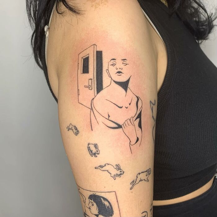 Illustration-style tattoo on arm depicting a figure near a door, with small rabbits around.