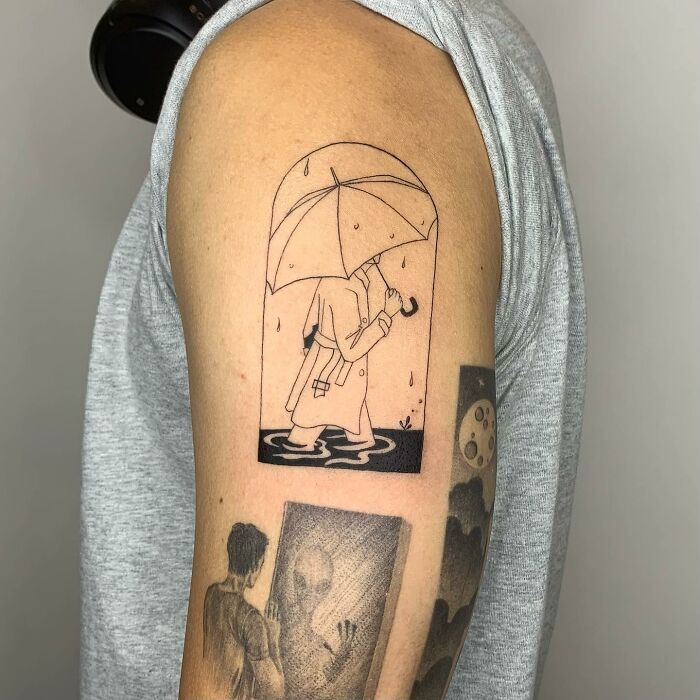 Tattoo illustration of a person with umbrella in the rain, drawn on upper arm.
