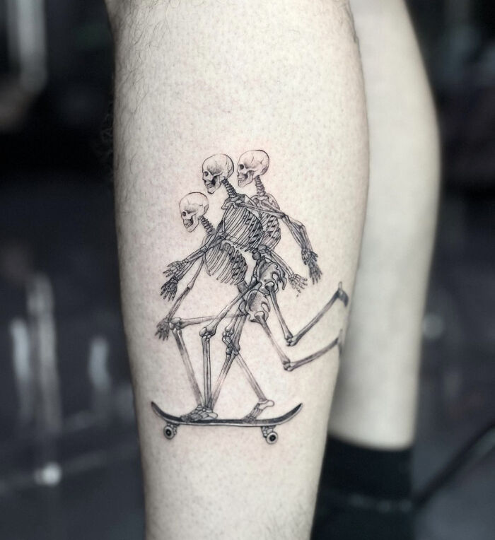 Skeleton tattoo on leg, depicting three figures on a skateboard, embodying dynamic movement.