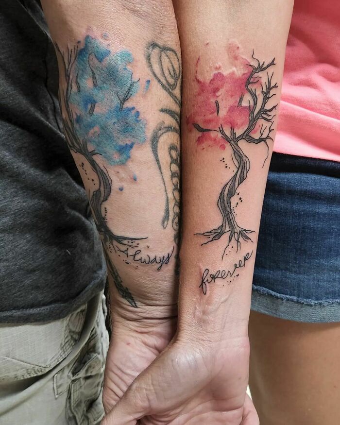 Matching tree tattoos on forearms with blue and red leaves, symbolizing connection for special people in your life.