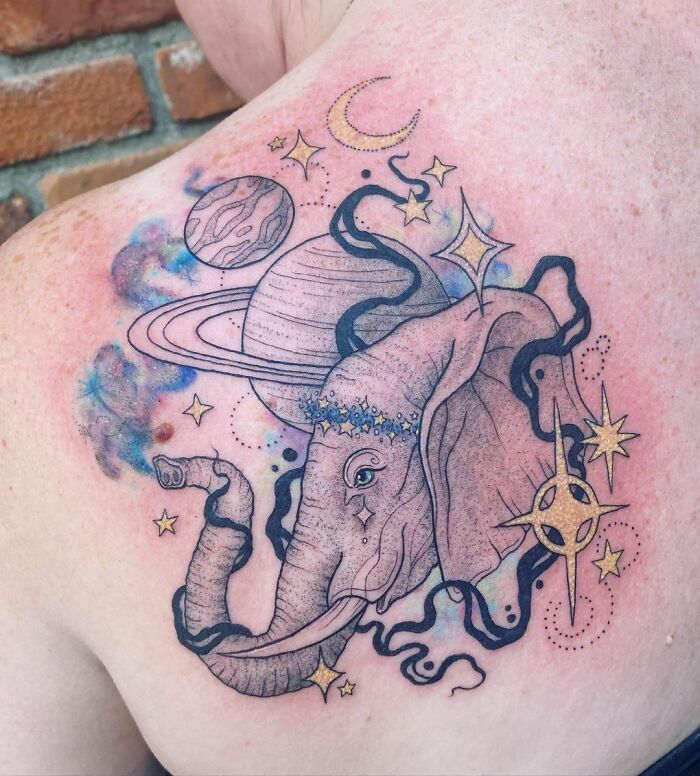 Space tattoo featuring an elephant with planets, stars, and cosmic elements on a person's shoulder.