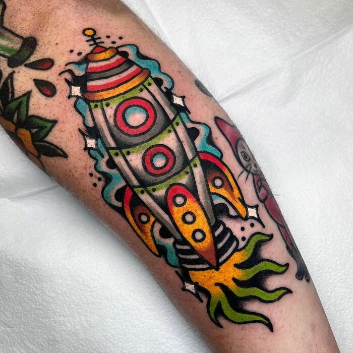 Colorful rocket space tattoo on forearm, featuring vibrant design elements for astrology fans.