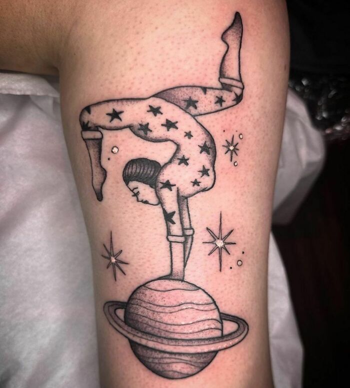 Space tattoo featuring a star-covered figure balancing on a ringed planet, surrounded by stars.