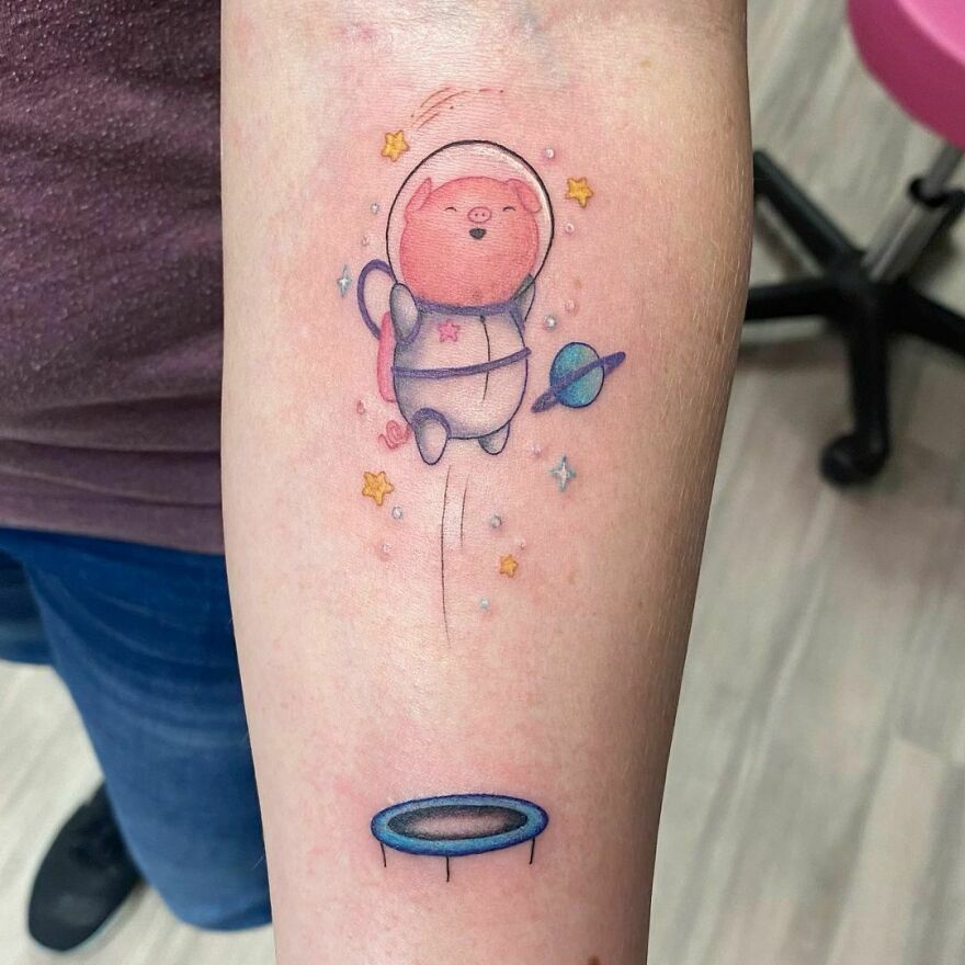 Cute space tattoo featuring an astronaut cat bouncing on a trampoline with stars and planets around it.