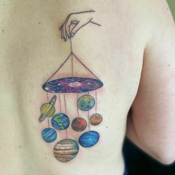 Space tattoo of hand holding planets on skin, featuring colorful cosmic design for astrology fans.