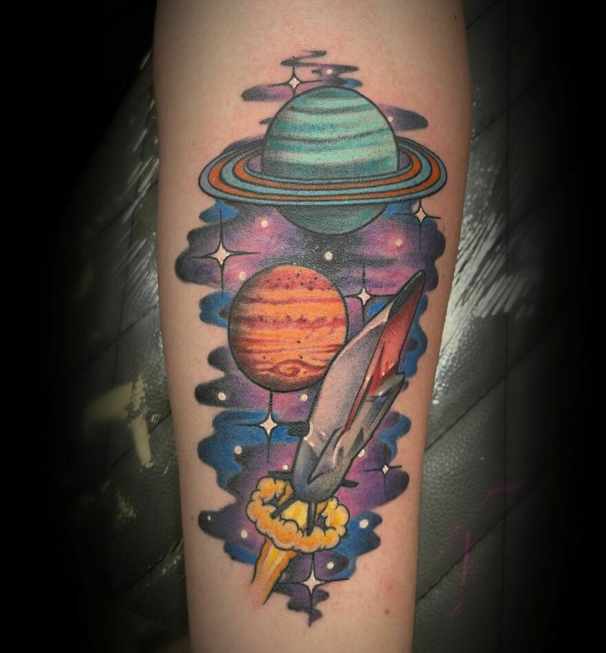 Space tattoo featuring vibrant planets and a rocket, showcasing a colorful outer space design on an arm.