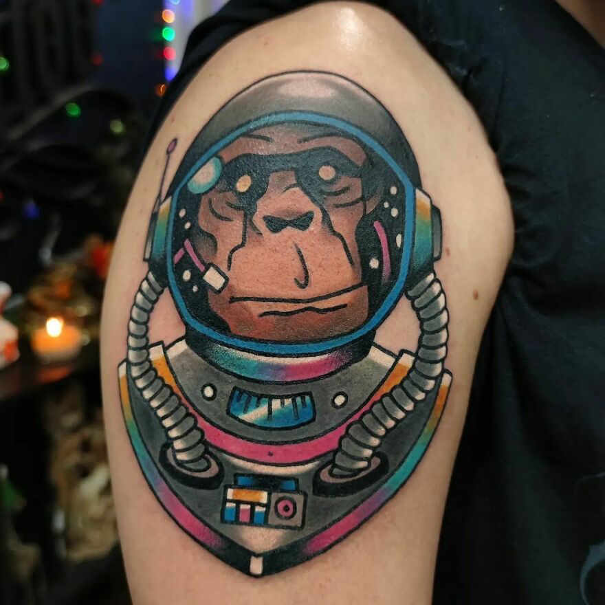 Space tattoo of a chimp in a colorful astronaut suit on an upper arm.