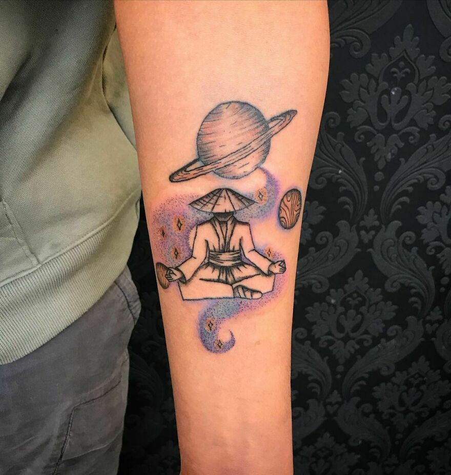 Space tattoo featuring a meditating figure with planets and swirling galaxy on forearm.