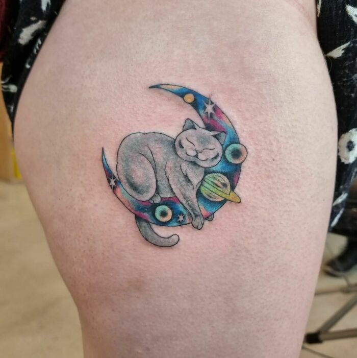 Space tattoo featuring a cat resting on a crescent moon with planets and stars.