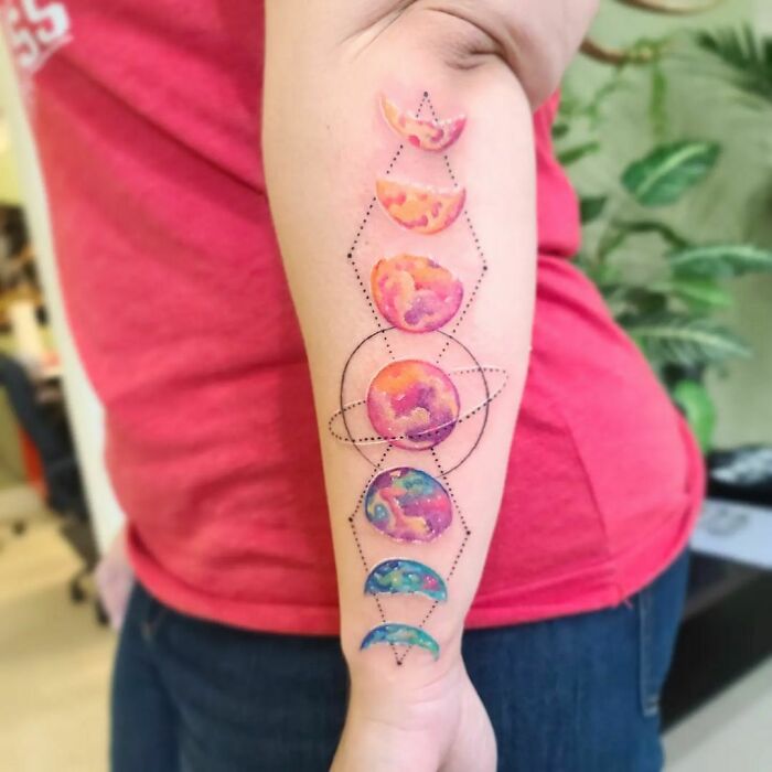 Colorful space tattoo with planets and moon phases on a forearm, perfect for astrology fans.