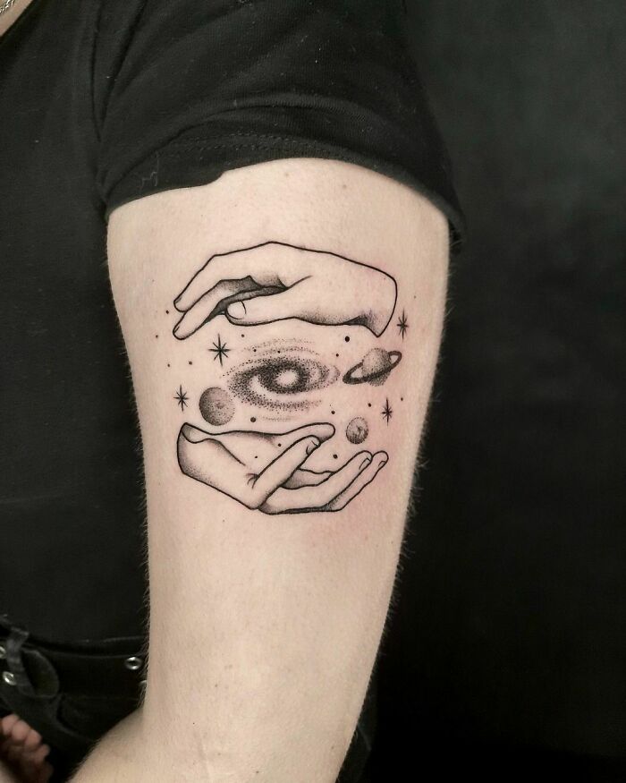 Space tattoo featuring hands holding planets and stars on an arm.