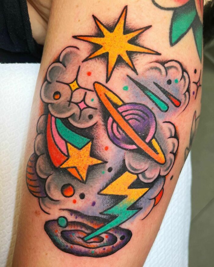 Colorful space tattoo featuring planets, stars, and clouds on an arm.