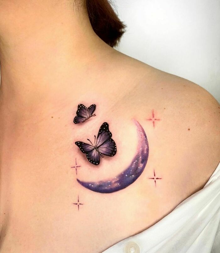 Elegant space tattoo featuring a crescent moon with two butterflies and stars on a person's shoulder.