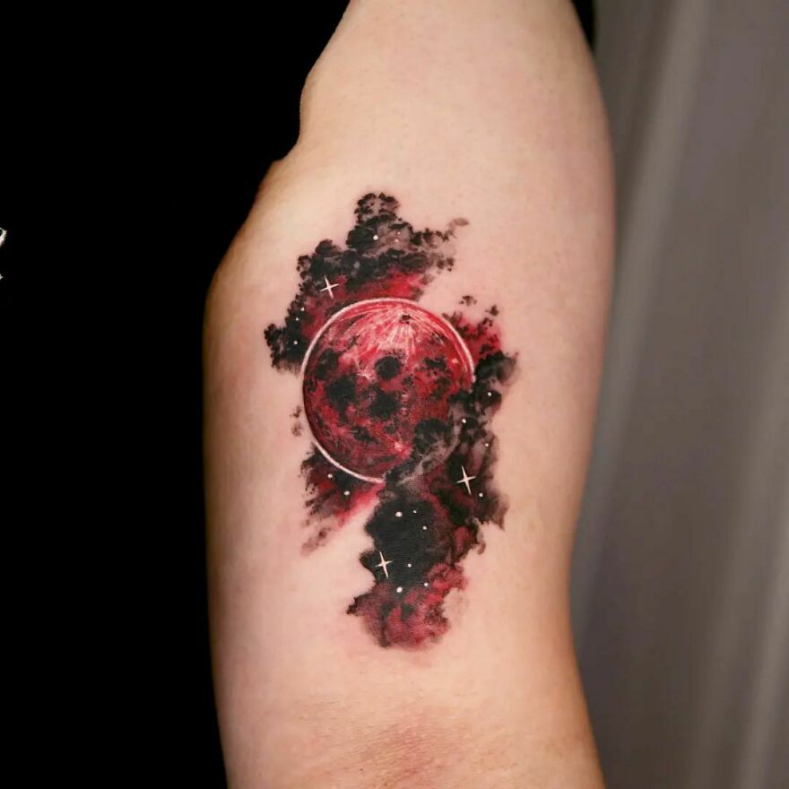 Space tattoo featuring a red planet surrounded by dark clouds and stars on a person's upper arm.