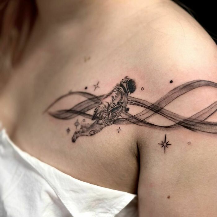 Astronaut space tattoo on upper arm with cosmic elements and swirling patterns.