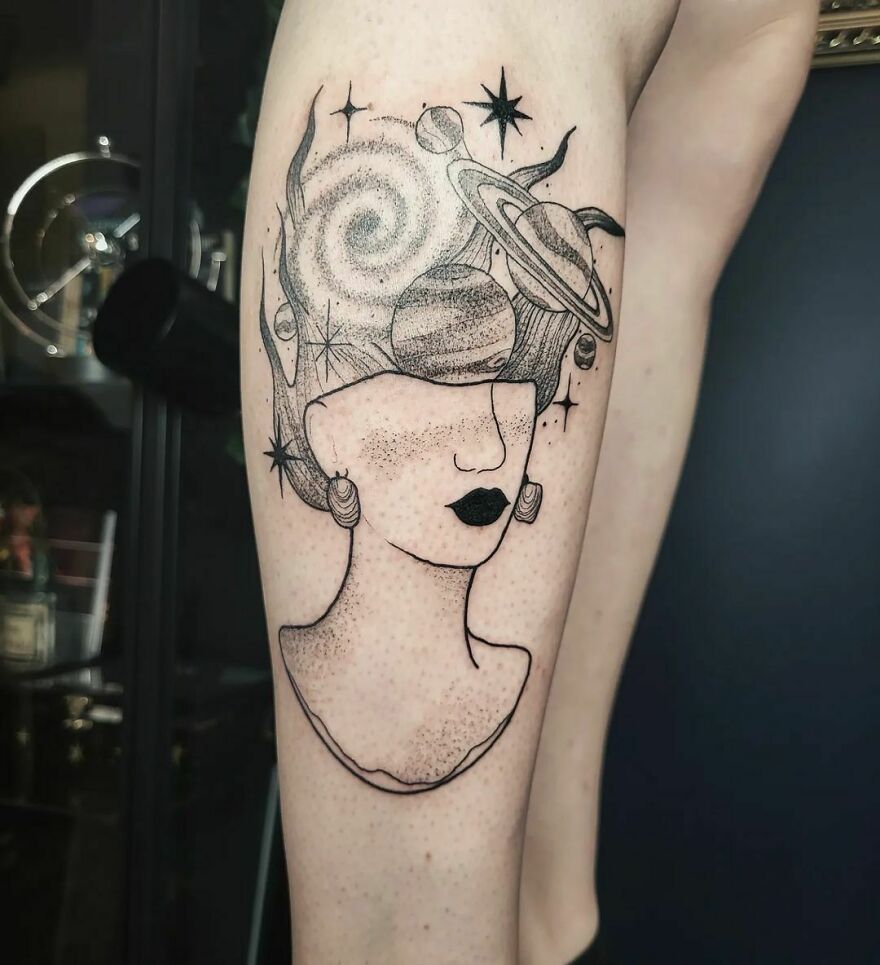 Stylized space tattoo featuring planets and stars integrated into a woman's head design on the leg.