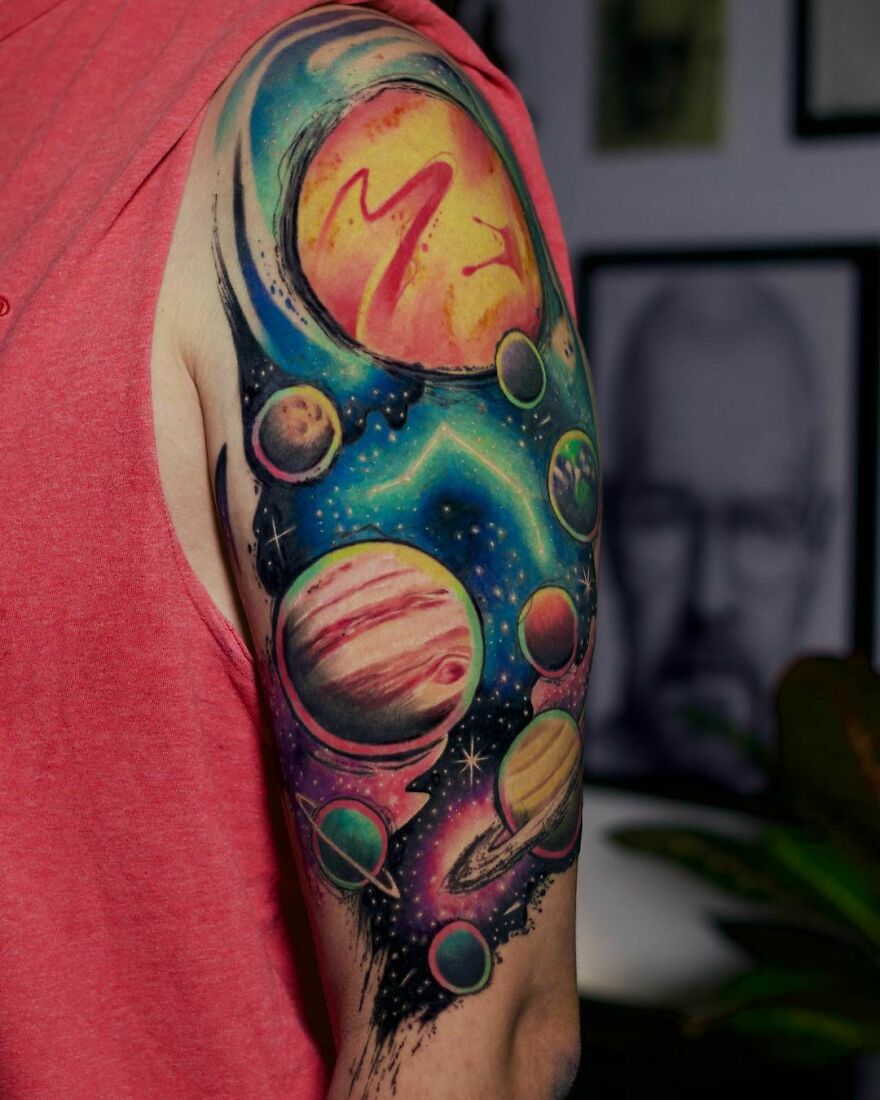 Colorful space tattoo featuring planets and stars on a person's upper arm, showcasing outer space design.