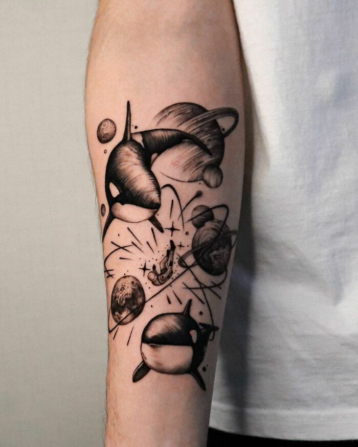 Space tattoo featuring orcas, planets, and an astronaut on a person's forearm, ideal for astrology enthusiasts.
