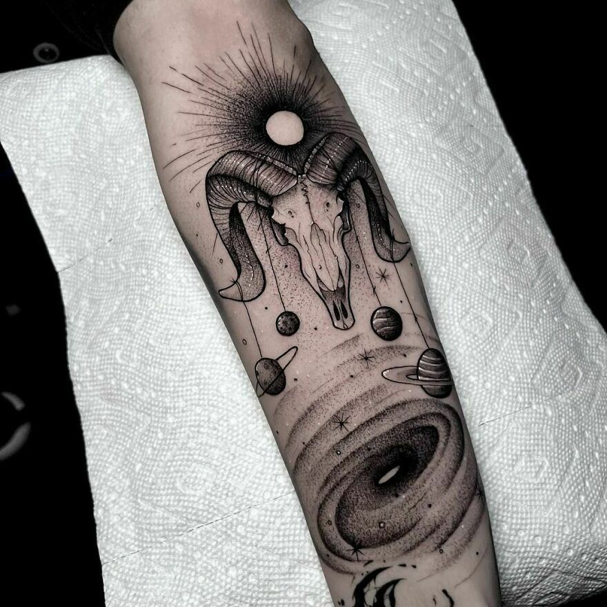 Space tattoo featuring a ram skull, planets, and a black hole on forearm.