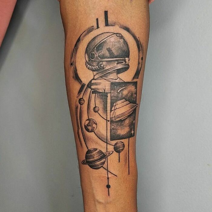 Space tattoo featuring an astronaut and planets on a forearm, showcasing cosmic art and a celestial theme.