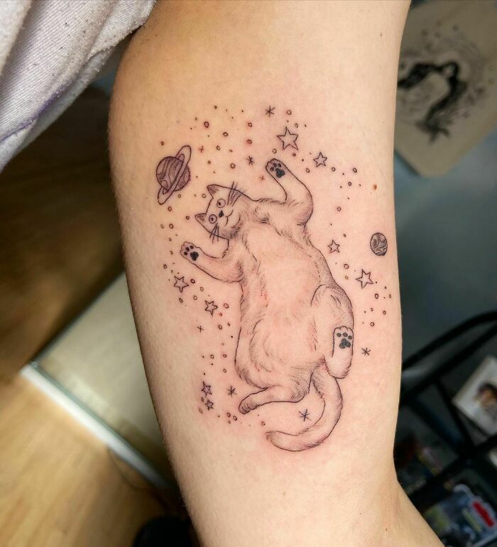 Space tattoos featuring a floating cat surrounded by stars and planets.