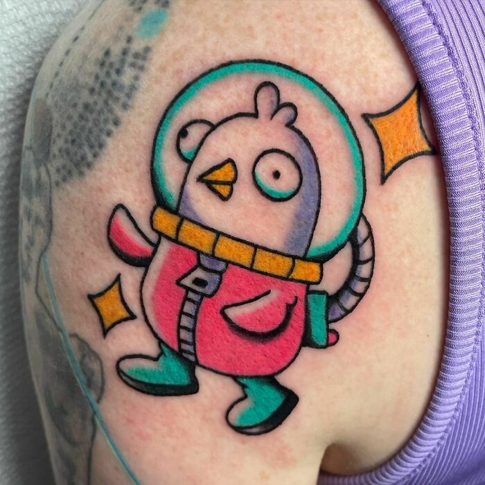 Cartoon chicken in a colorful spacesuit tattoo, showcasing a cool space theme on an arm.