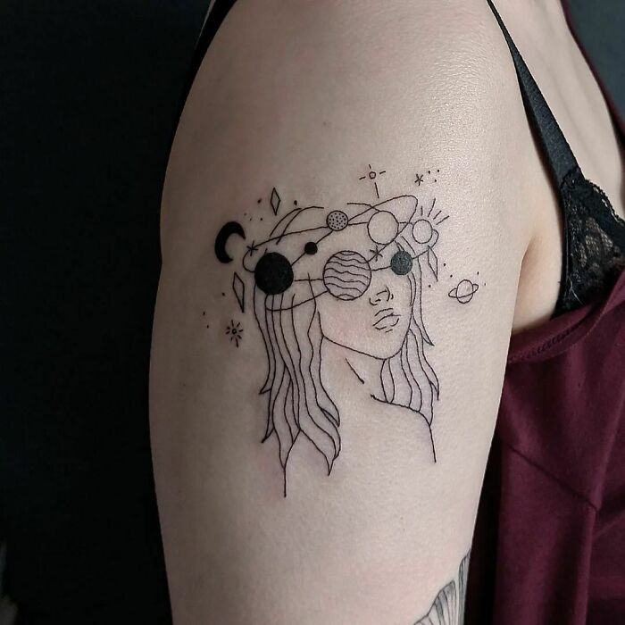 Minimalist space tattoo on arm featuring a woman's face adorned with planetary designs.