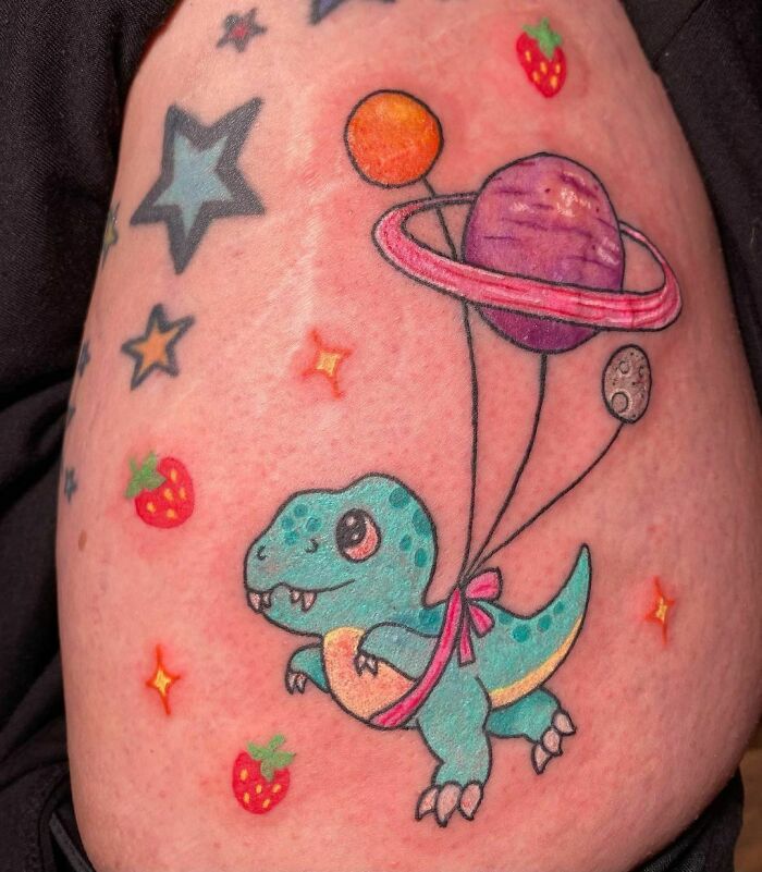 Colorful space tattoo with planets and stars featuring a dinosaur and strawberries.