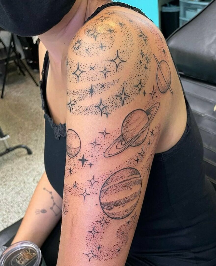 Space tattoo featuring planets and stars on a person's arm, showcasing outer space design.