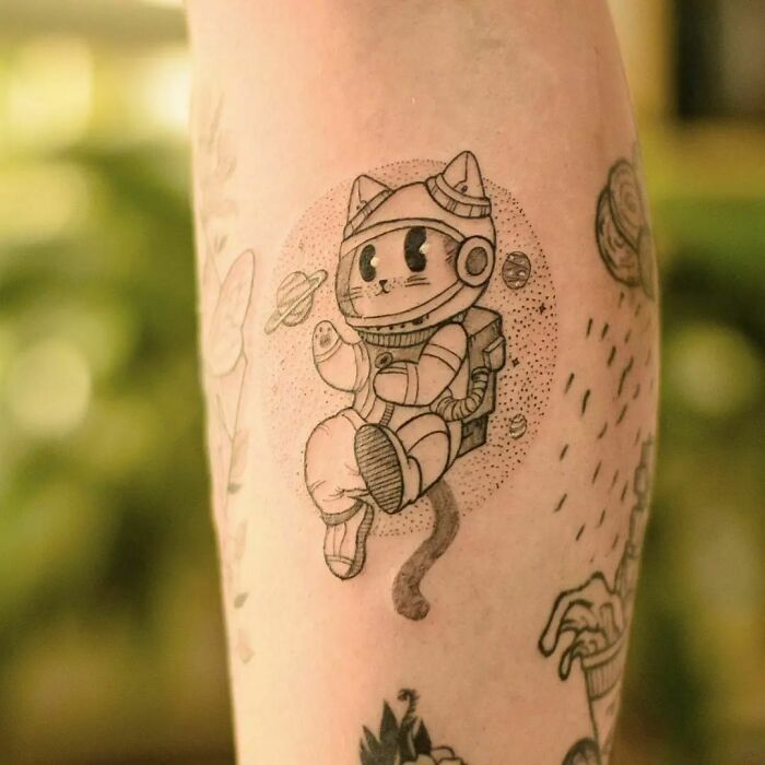 Cat astronaut space tattoo on arm with planets in the background.