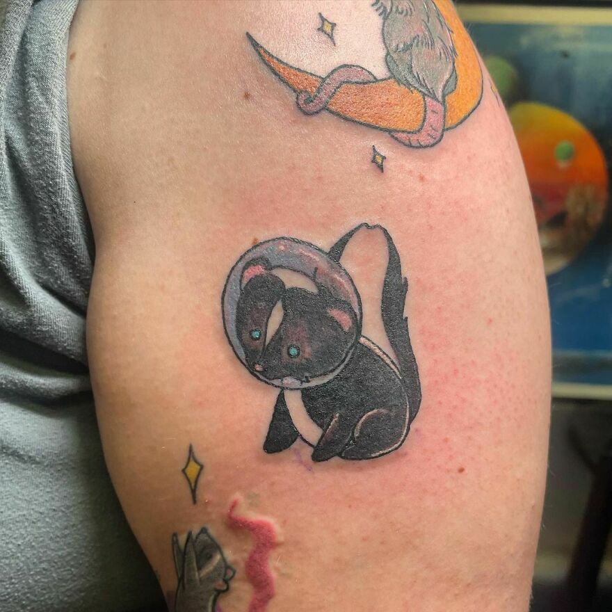 Tattoo of a skunk in a spacesuit on an arm, representing a quirky take on space-themed tattoos.