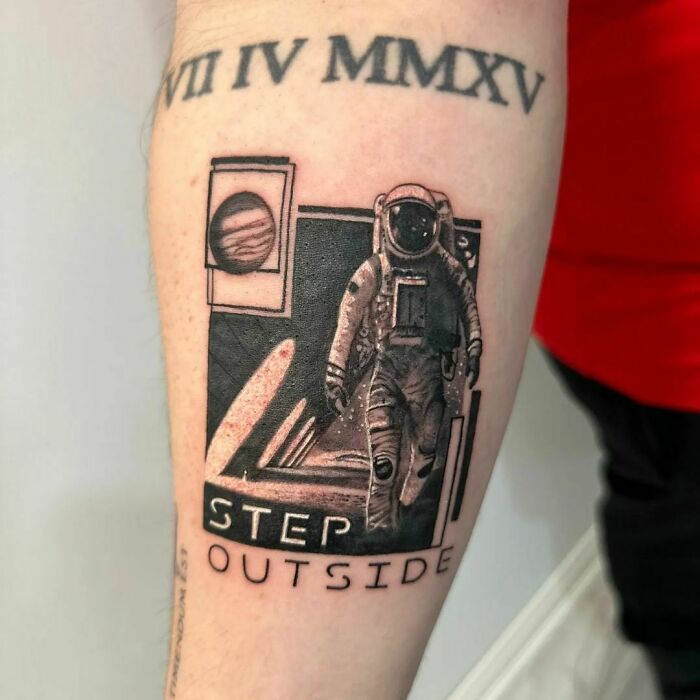 Space tattoo featuring an astronaut and the phrase "Step Outside" on a forearm, with Roman numerals above.